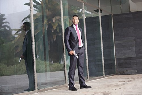 man in business suit standing in front of a building with gun in hand, presumably about to kill someone