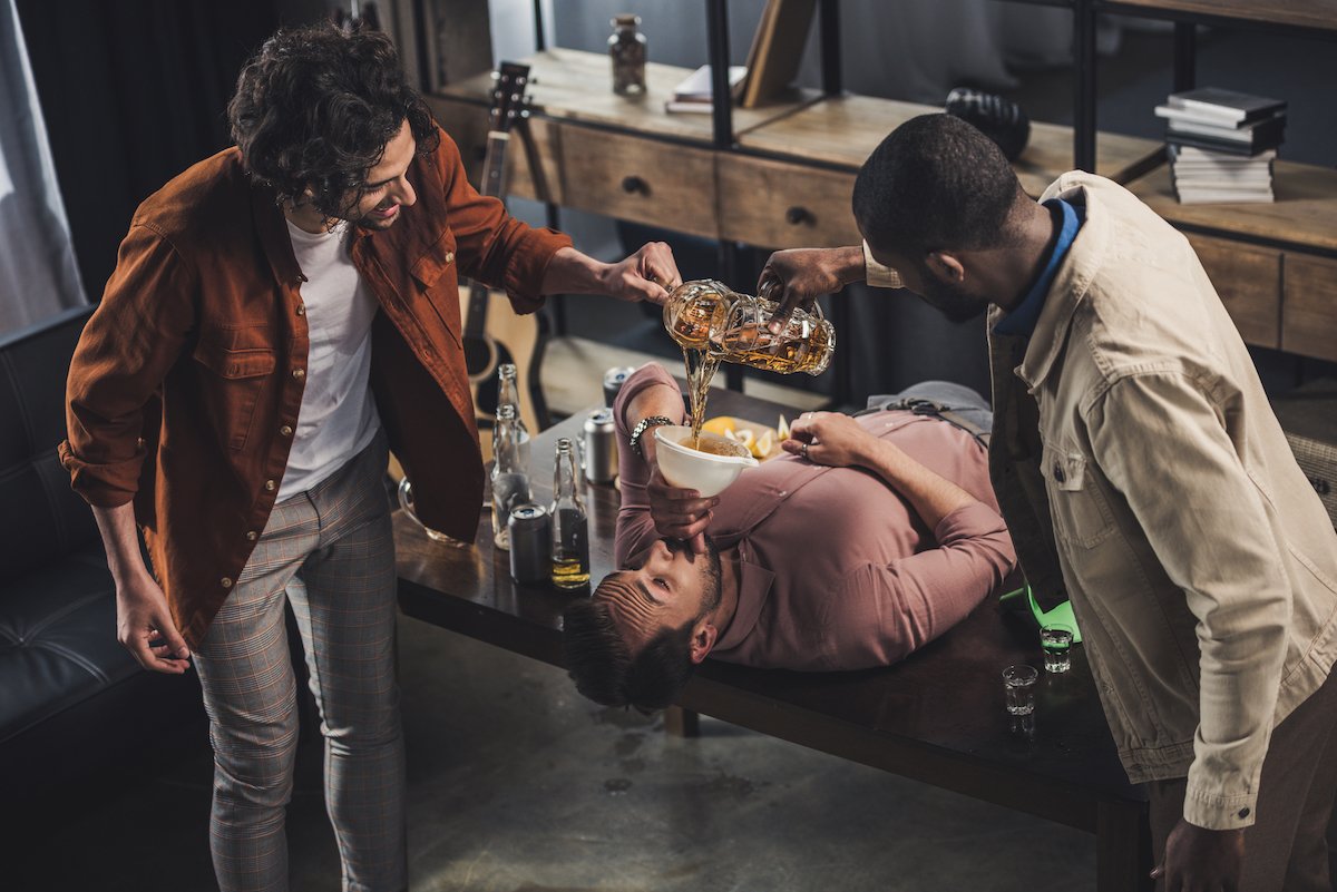 Tres estudiantes universitarios participando en un ritual de iniciación forzando el consumo de cerveza.
