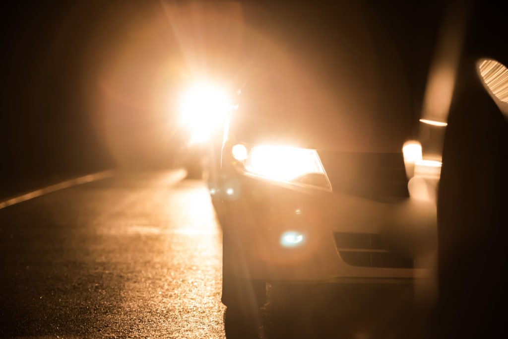 Un coche justo detrás de otro coche, y el coche trasero tiene las luces altas encendidas ilegalmente.