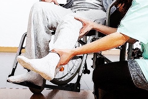 una enfermera atendiendo la pierna de un paciente lesionado en una silla de ruedas