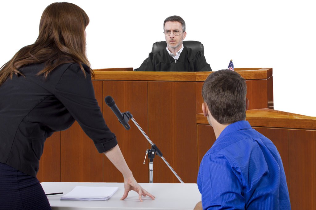 Judge in background with defense attorney and defendant in foreground in courtroom