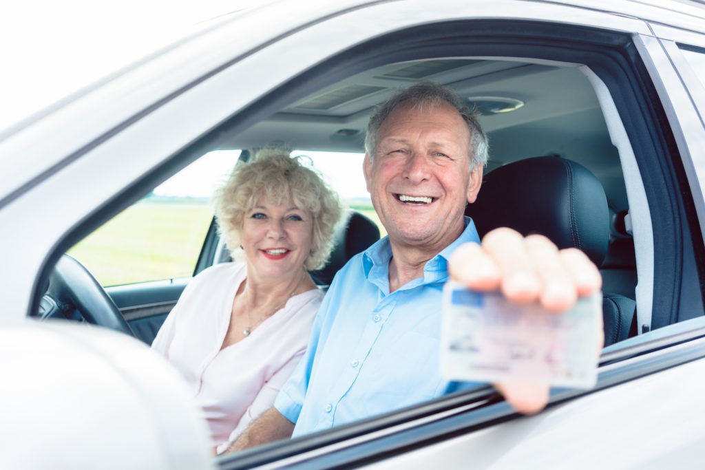 Conductores de edad avanzada mostrando su licencia en un coche.
