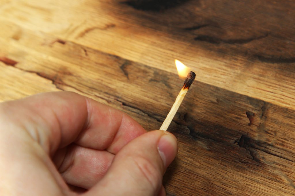 Hand holding lit match over wood