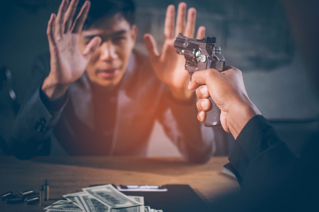 Mano sosteniendo un arma en dirección a una víctima como ejemplo de extorsión según el Código Revisado de Colorado 18-3-207