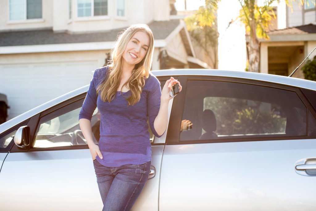 Mujer sonriente parada junto a su auto sosteniendo sus llaves