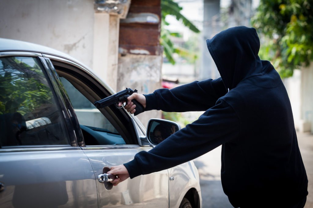 Ladrón con capucha apuntando con un arma a un vehículo