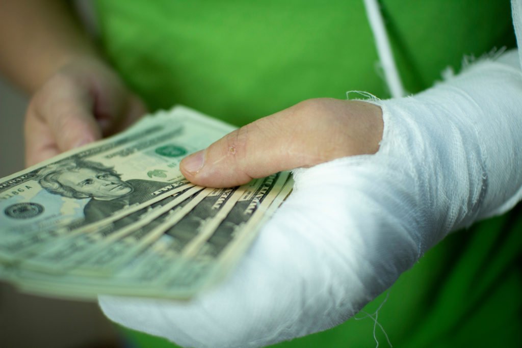 Hombre con brazo en yeso sosteniendo un puñado de billetes de $ 20 para ejemplificar los daños compensatorios en California