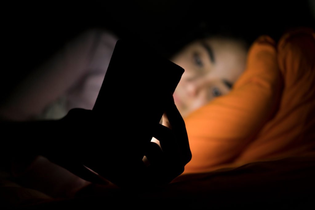 Niña en la cama iluminada por la luz de su teléfono