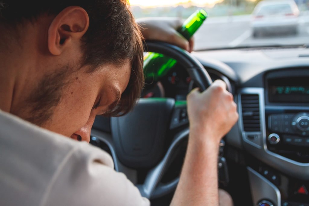 Hombre dormido al volante sosteniendo botella de cerveza