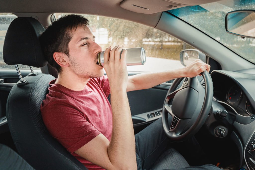 Hombre joven intoxicado bebiendo cerveza mientras conduce y un ejemplo de una violación del Código de Vehículos 23152(a) VC