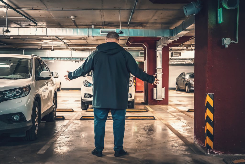 Hombre parado en un lugar de estacionamiento vacío en un garaje subterráneo - hacer un informe falso de robo de auto es un delito en California