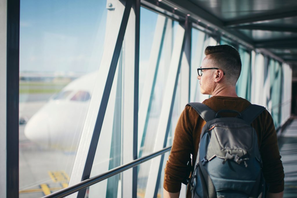 Traveler with backpack looking out of airport gate window at plane