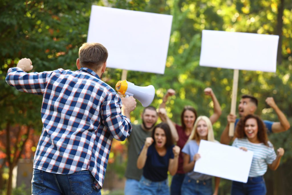 Hombre con megáfono hablando con manifestantes con carteles.