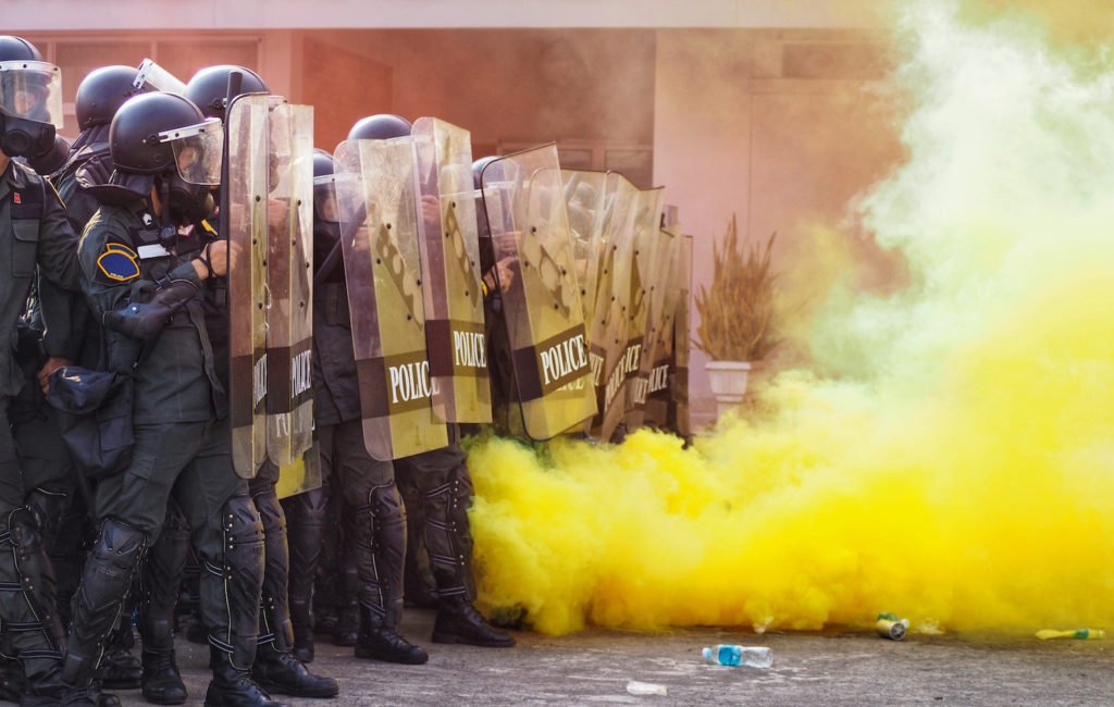 Wall of shielded police releasing tear gas into unlawful assembly