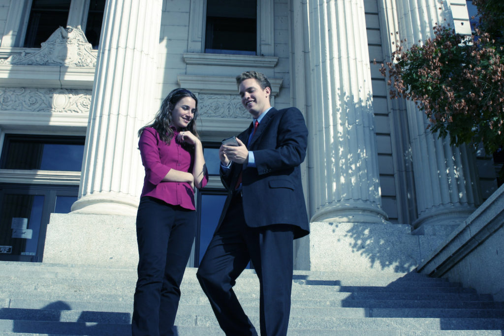 Attorney and client outside courthouse steps checking case status on phone