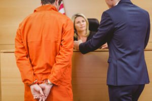 Abogado en el banquillo hablando con el abogado de la defensa y el acusado en traje de preso