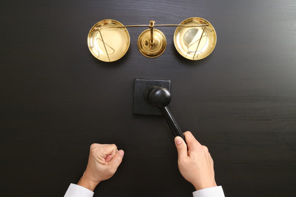 Hands holding a gavel in front of a scale of justice