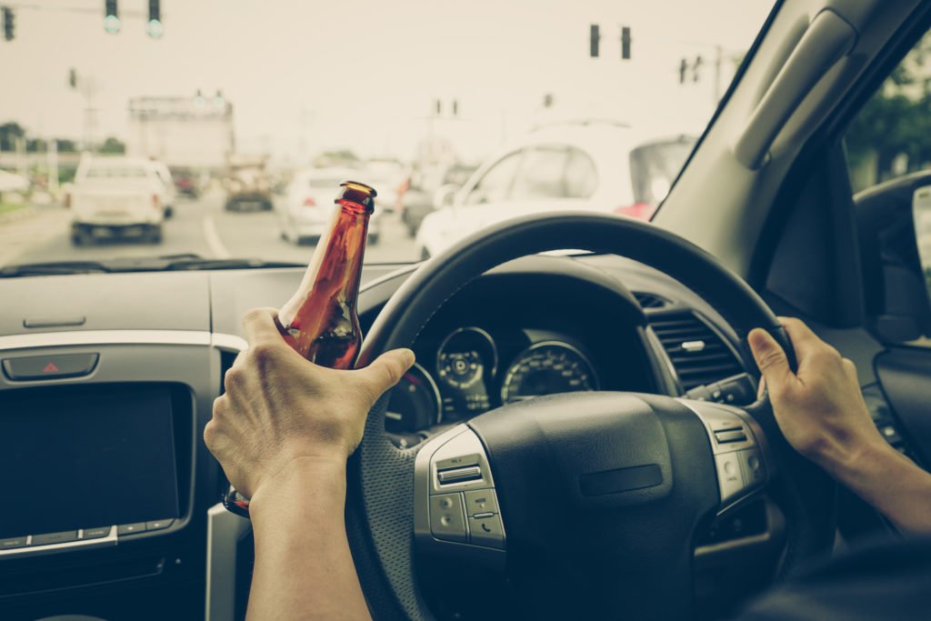 Manos en el volante mientras sostiene una botella de cerveza