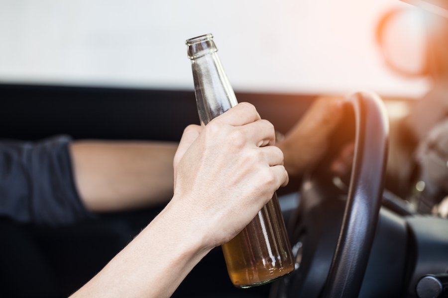 Hand on steering wheel holding beer