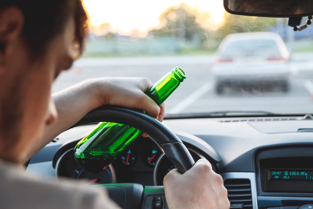 Man holding beer bottle while asleep at the wheel
