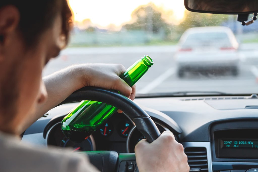 Hombre sosteniendo una botella de cerveza mientras duerme al volante