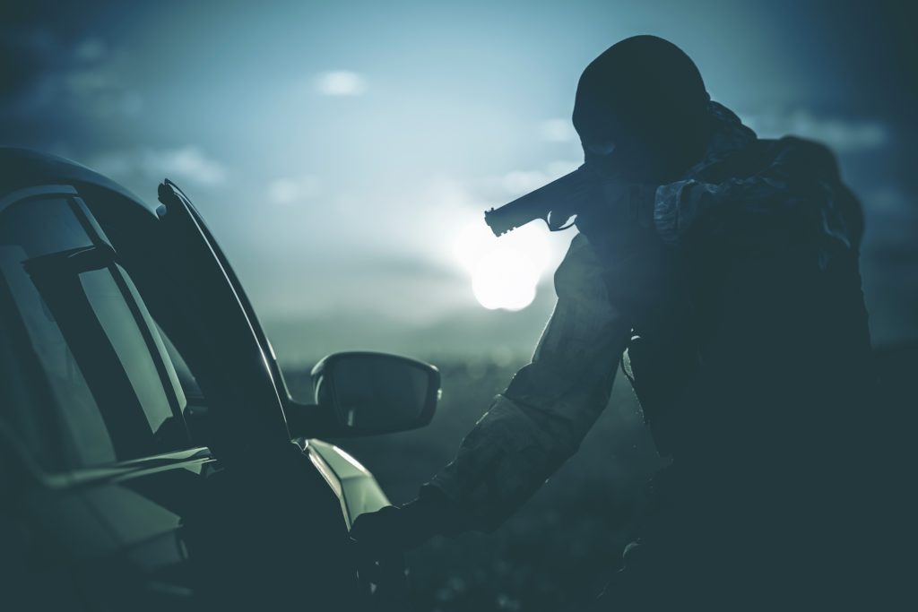 Silueta de un hombre apuntando con un arma a un automóvil como ejemplo de descarga ilegal de un arma de fuego