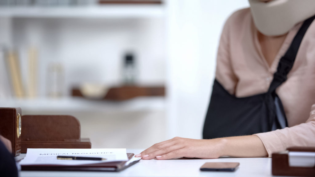 Woman with neck brace and sling at desk applying for workers' comp