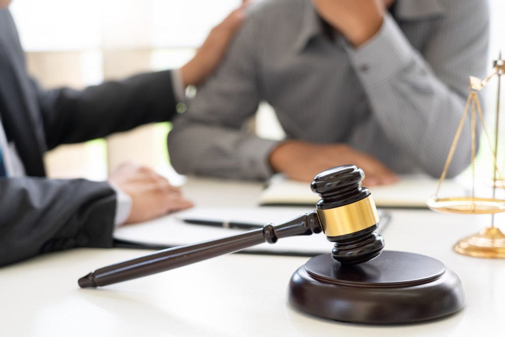 Attorney comforting client with gavel and a scale of justice in the foreground