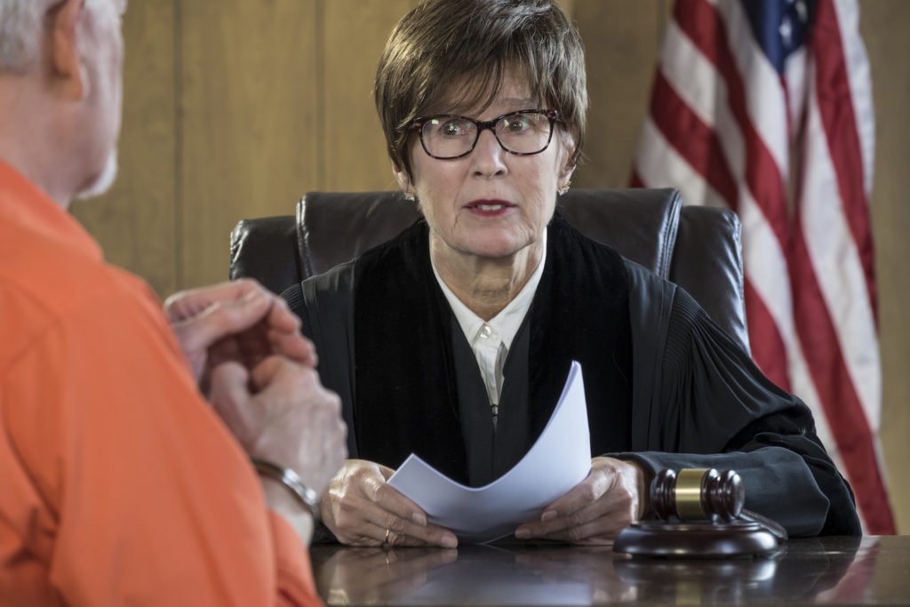 Judge with gavel speaking to defendant in jumpsuit