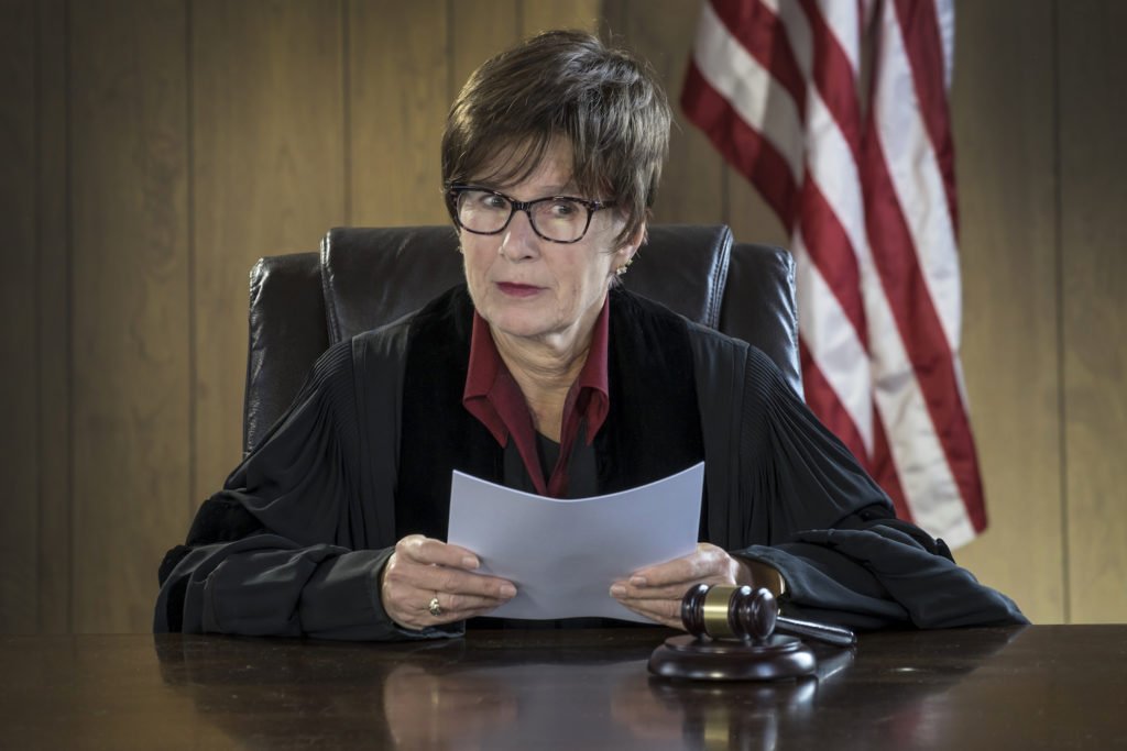 Judge holding paper at bench with flag in background