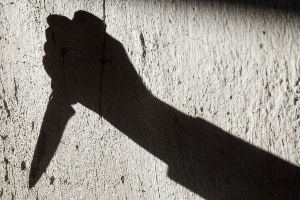 Shadow of a hand wielding knife cast on a concrete wall