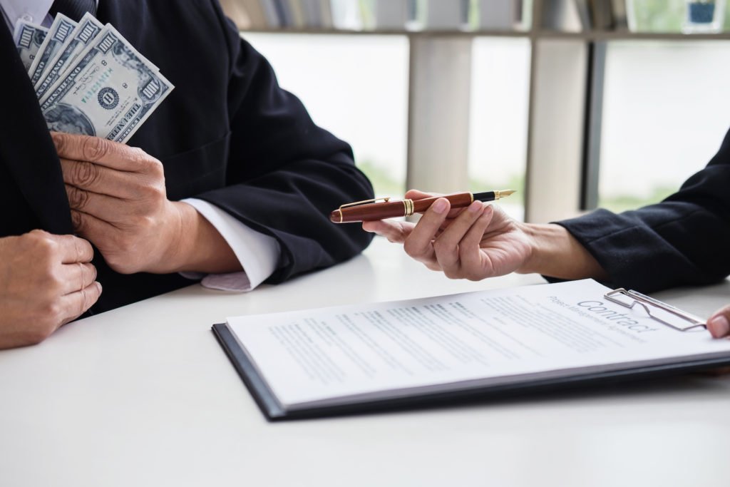 Man in suit pocketing cash at desk with clipboard