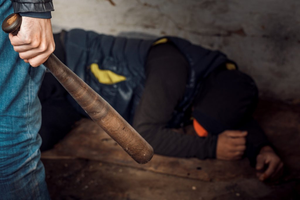 Man with baseball bat about to hit cowering victim on floor