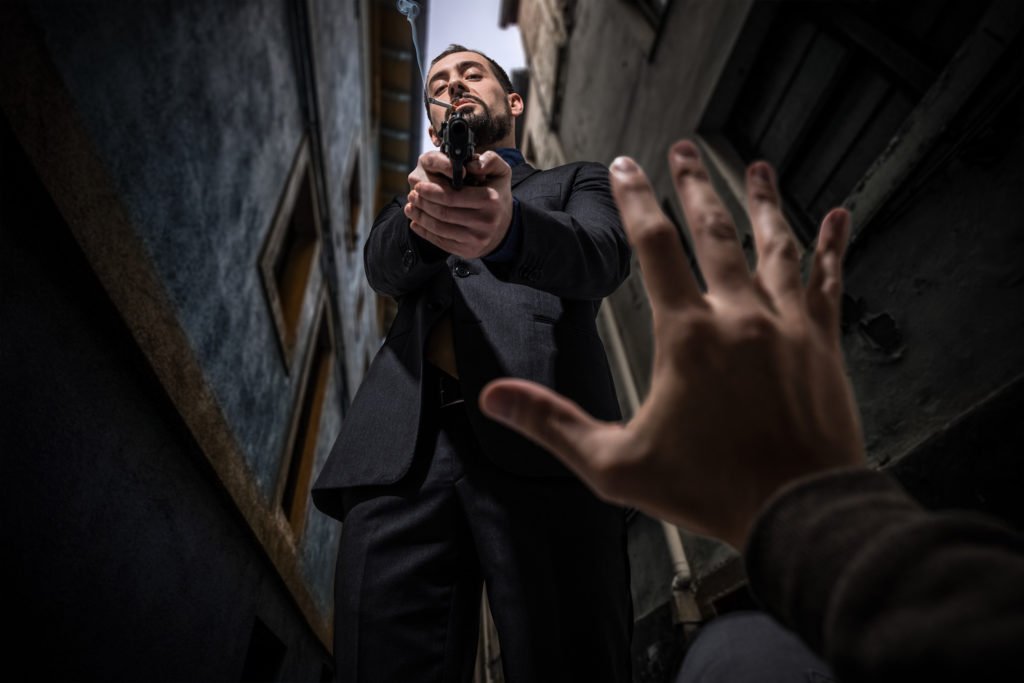 Man aiming gun at victim on ground raising his hand in alleyway