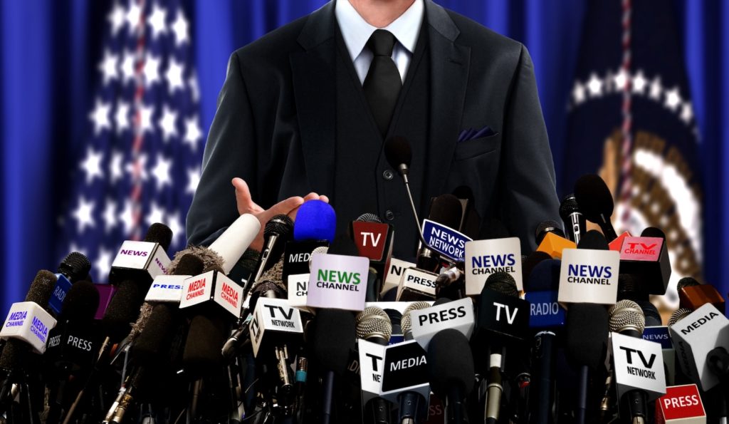 Federal government official being interviewed with American flag in background