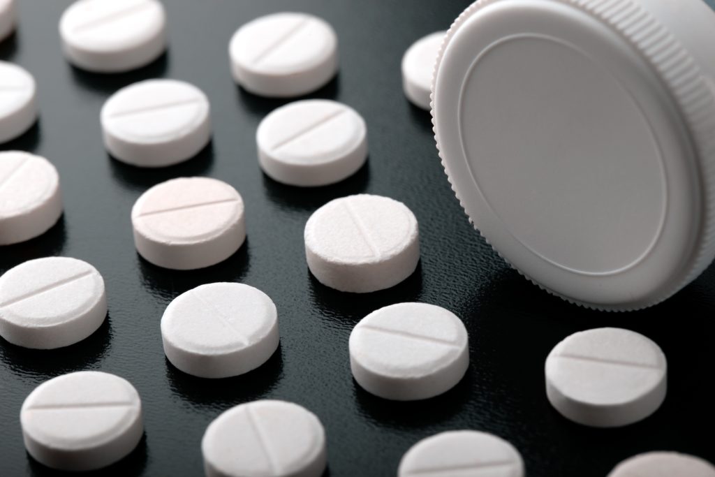 Pills lined up on a table with a pill bottle on its side