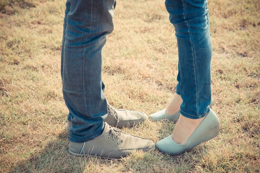 Man's legs near young woman's legs on tiptoes, indicating that they are kissing out of frame