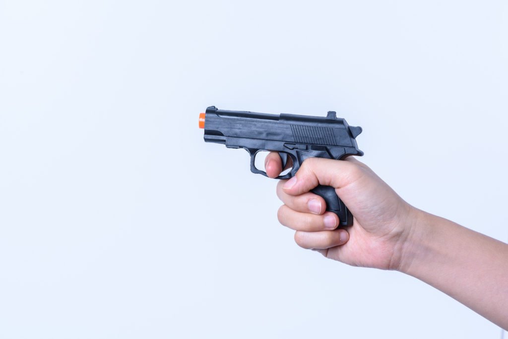Mano apuntando una pistola de juguete como ejemplo de exhibir un arma de imitación en violación del Código Penal 417.4 PC