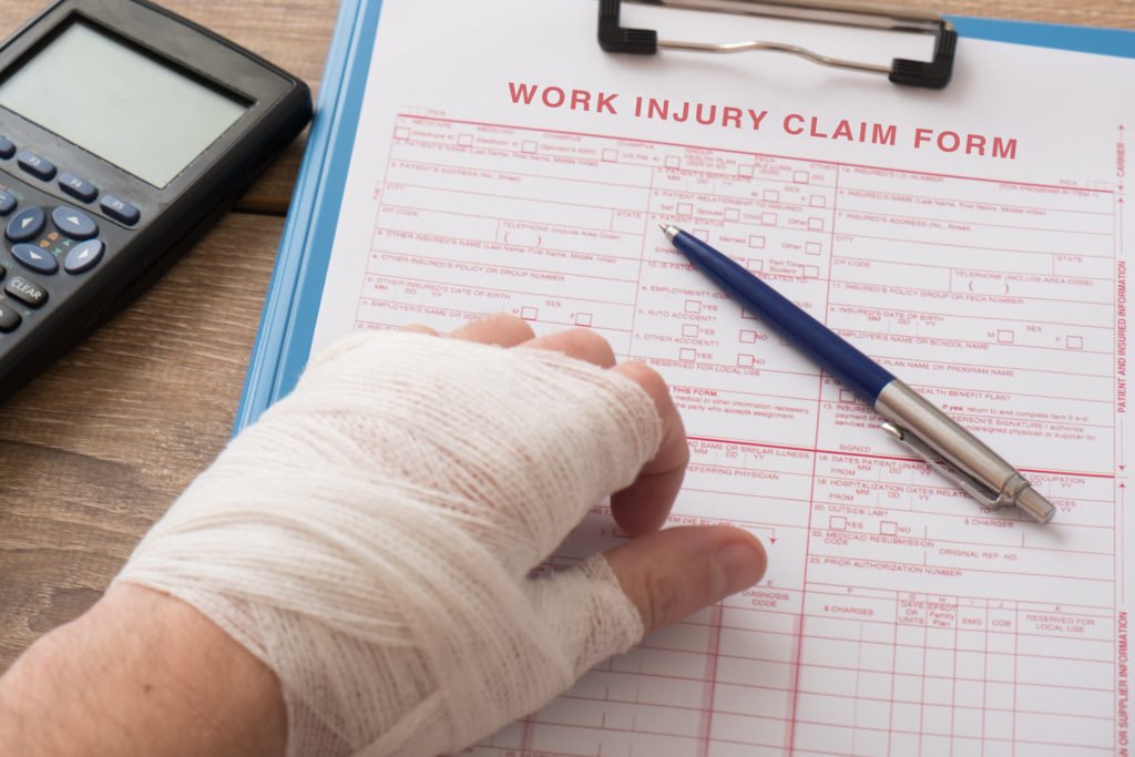 Hand wrapped in gauze filling out workers' comp claim form with pen and calculator