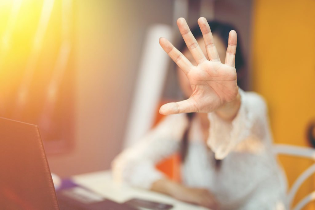 Woman at workdesk holding hand out to deflect attack