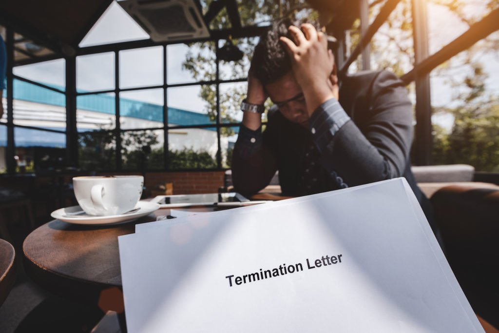 Distraught employee at coffee table with termination letter in foreground