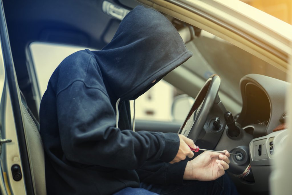 Ladrón encapuchado sentado en el asiento del conductor intentando encender un auto como ejemplo de una violación del CRS 18-4-409 de Colorado