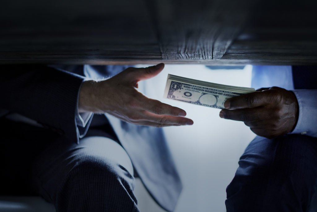 Close up of public official taking solicited money under a table in violation of CRS 18-8-304 