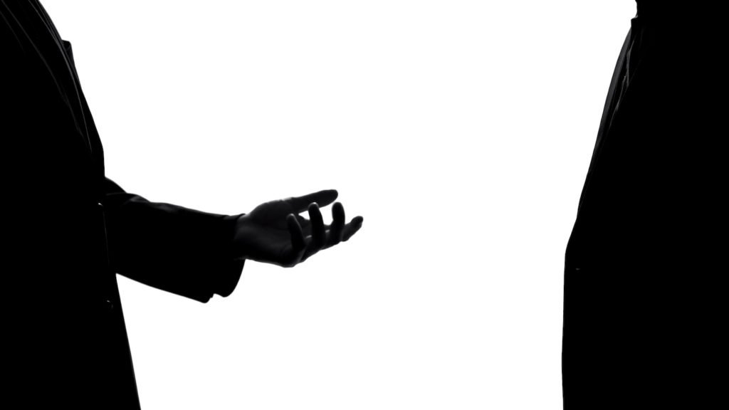Silueta de un hombre extendiendo la mano a otro hombre como ejemplo de intento de extorsión en California según el Código Penal 524 PC