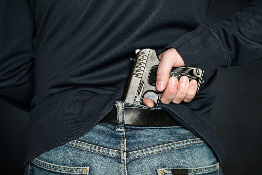 Hombre con revólver en la parte trasera de la cintura como ejemplo de posesión de un arma por un delincuente anterior en Colorado