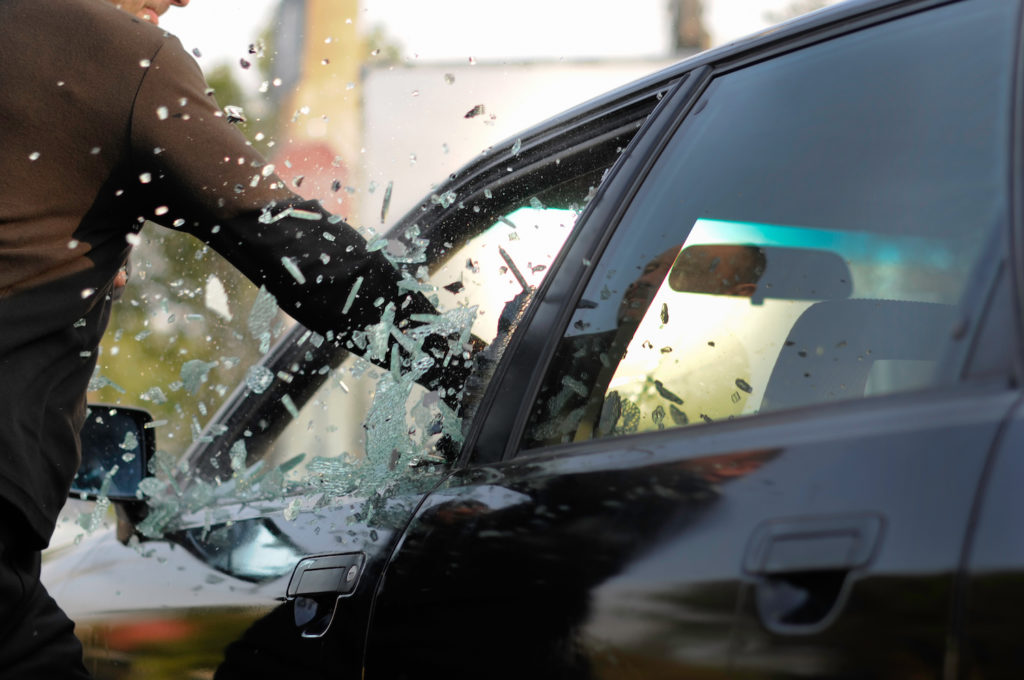 Hombre rompiendo la ventana de un auto como ejemplo de daño criminal en violación de CRS 18-4-501 de Colorado