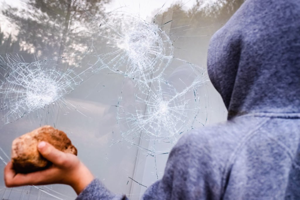 Hooded person with rock in hand being used to break a window