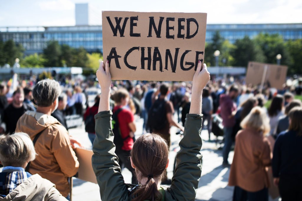 Manifestante político sosteniendo un cartel que dice 'Necesitamos un cambio', lo cual no sería un motivo legal para despedir al manifestante en California