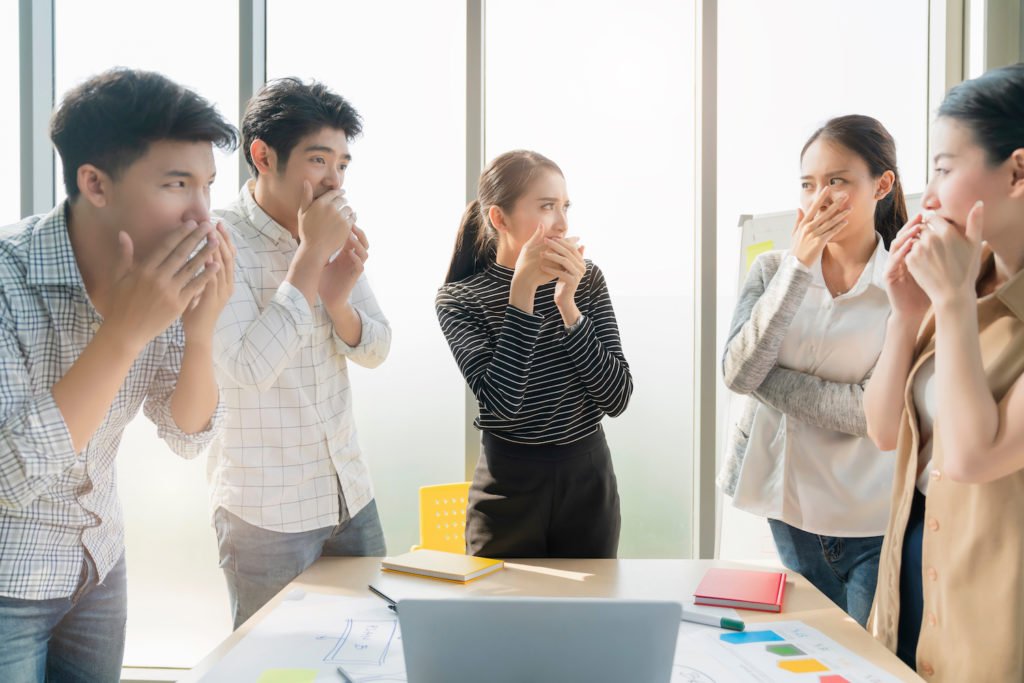 Office workers around a desk holding their noses