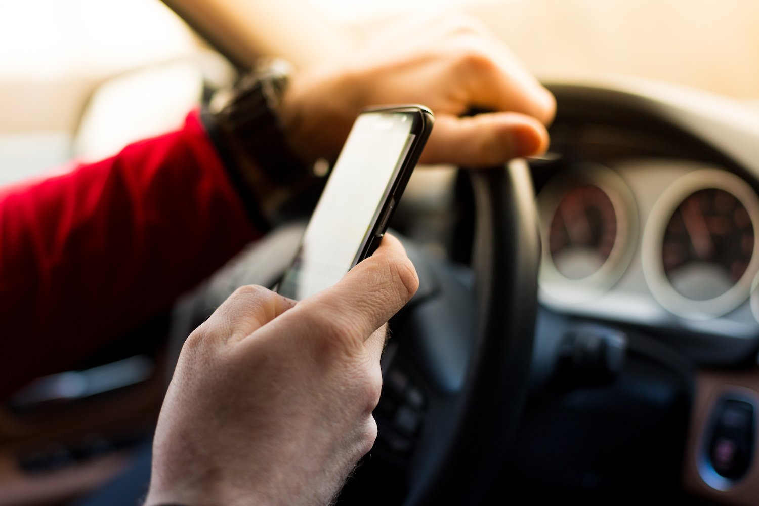 Close up of hand texting while other hand on steering wheel